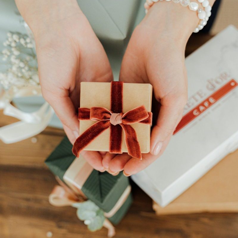 A close-up of hands holding a beautifully wrapped gift box with a velvet ribbon.