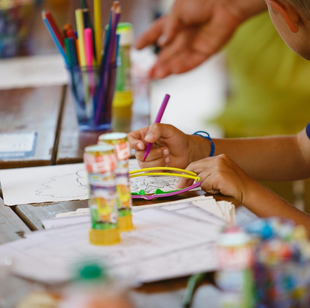 A young child focused on a drawing activity at a colorful art table indoors.